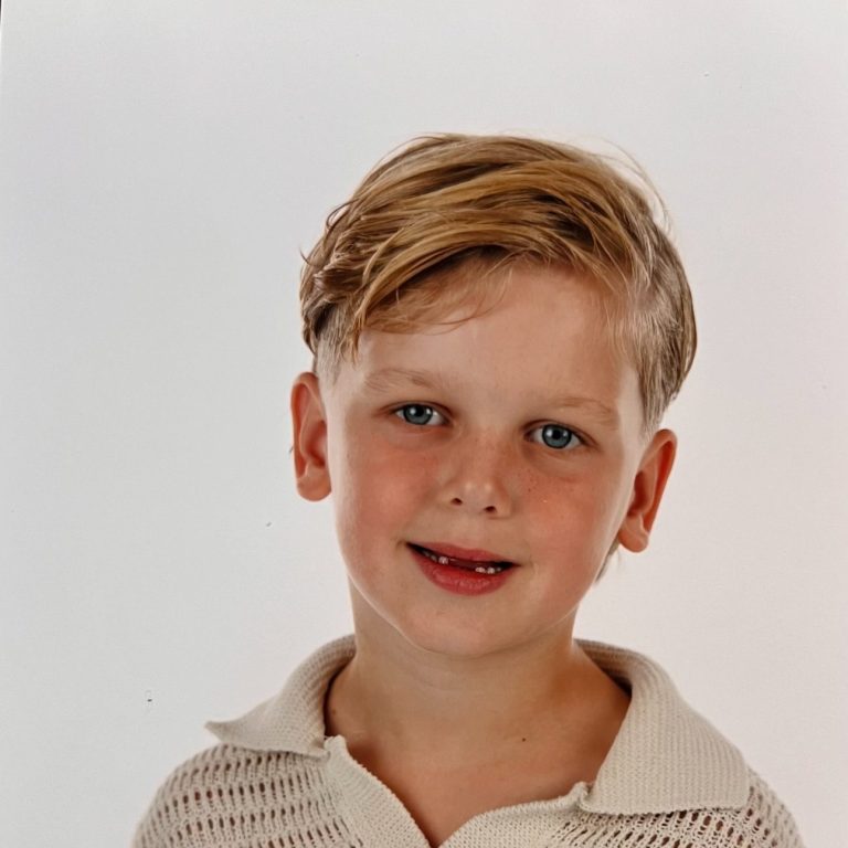 Jongentje met blond haar en blauwe ogen, glimlachend in een lichte omgeving.