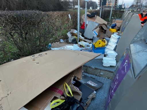 Rommel en afval, waaronder karton en plastic, langs een straat.