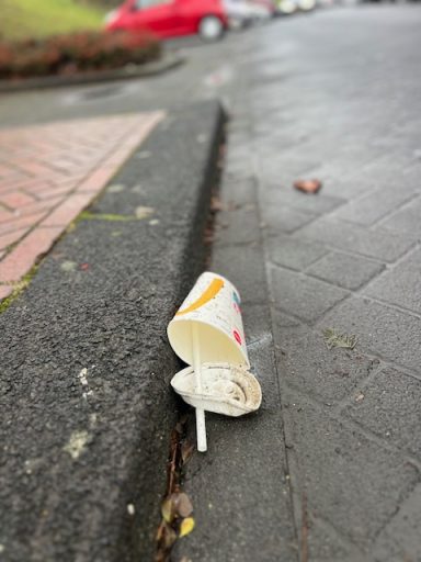 Vervuiling op de stoep: een omgevallen bekertje met een rietje naast de rand.