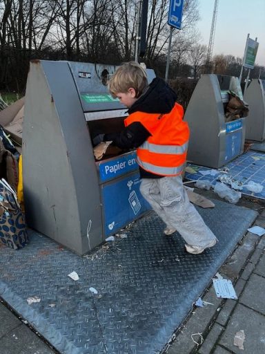 Jongen in een oranje hesje gooit afval in een recyclingcontainer.