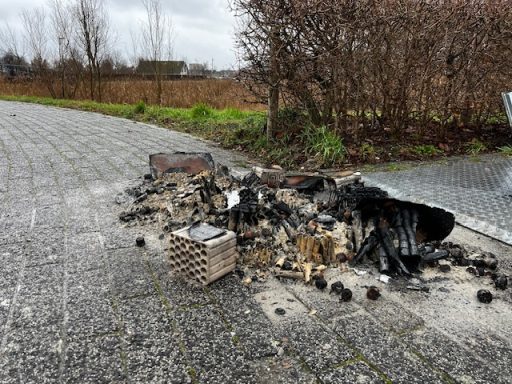 Afvalhoop met verbrande materialen en rommel langs een kiezelweg.