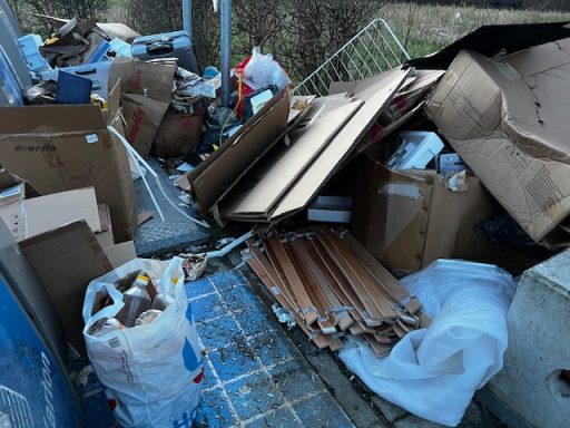 Afvalhoop met dozen, plastic en andere rommel op een onverzorgde locatie.